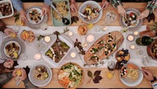 Overhead shot of a vibrant dining table setup with pasta, salads, and decorative candles, capturing a festive gathering.